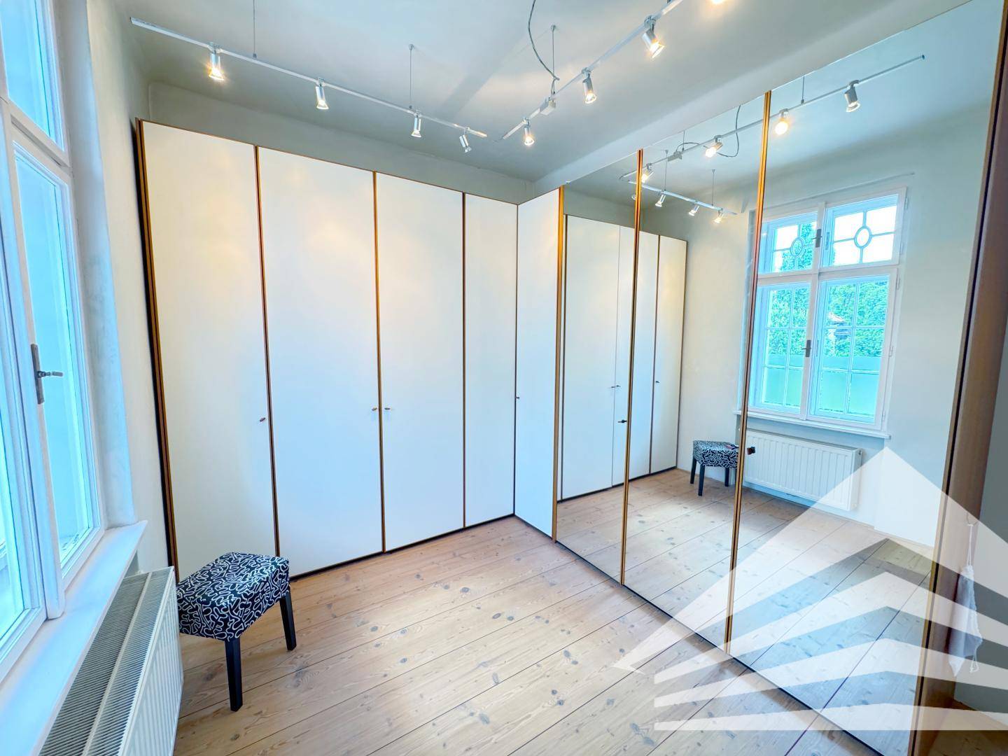 Schlafzimmer mit Einbauschränken, Spiegelwand und Holzdielenboden.