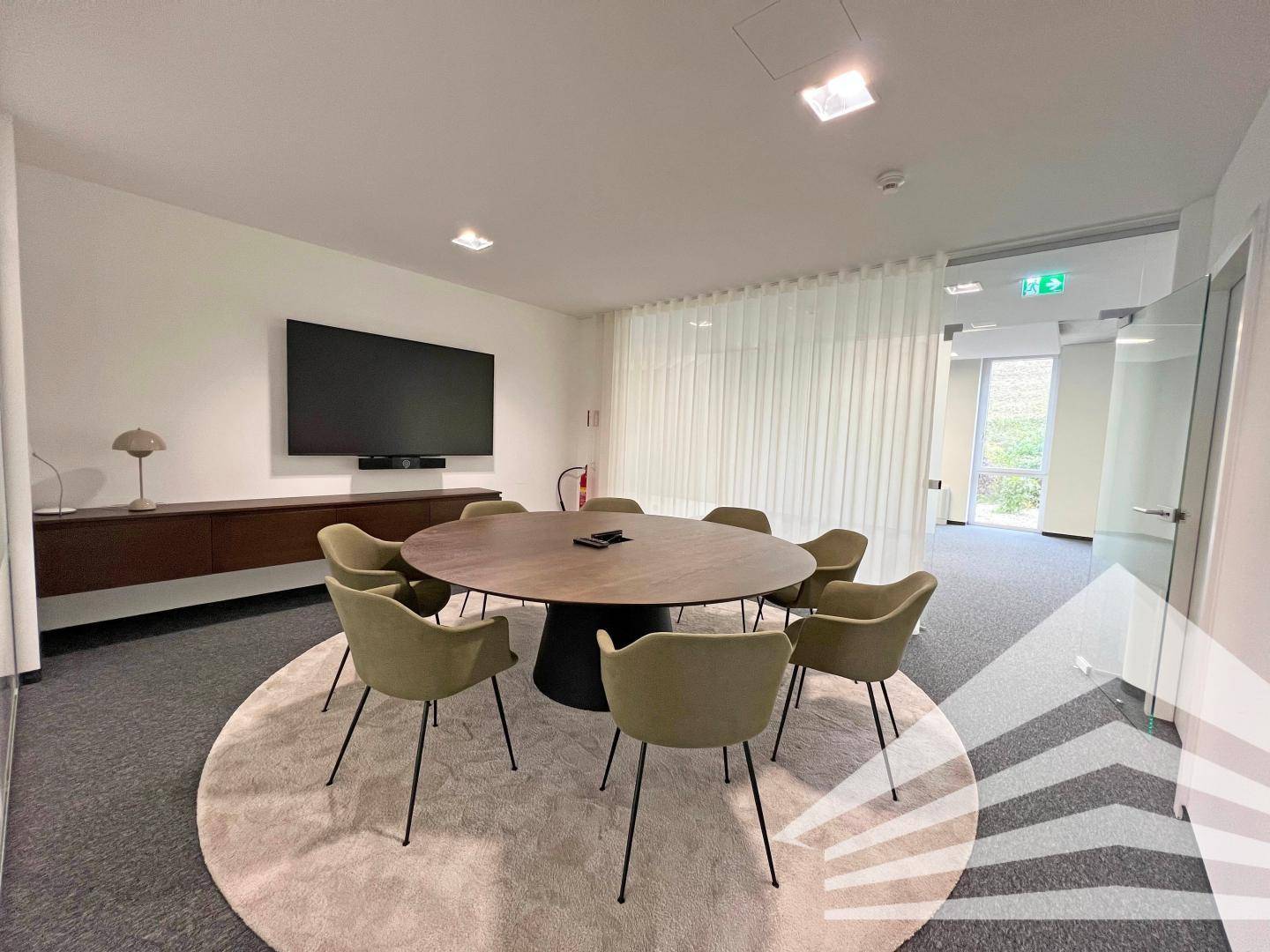 Moderner Konferenzraum mit elegantem runden Tisch, bequemen Stühlen und großem Bildschirm für effektive Meetings.