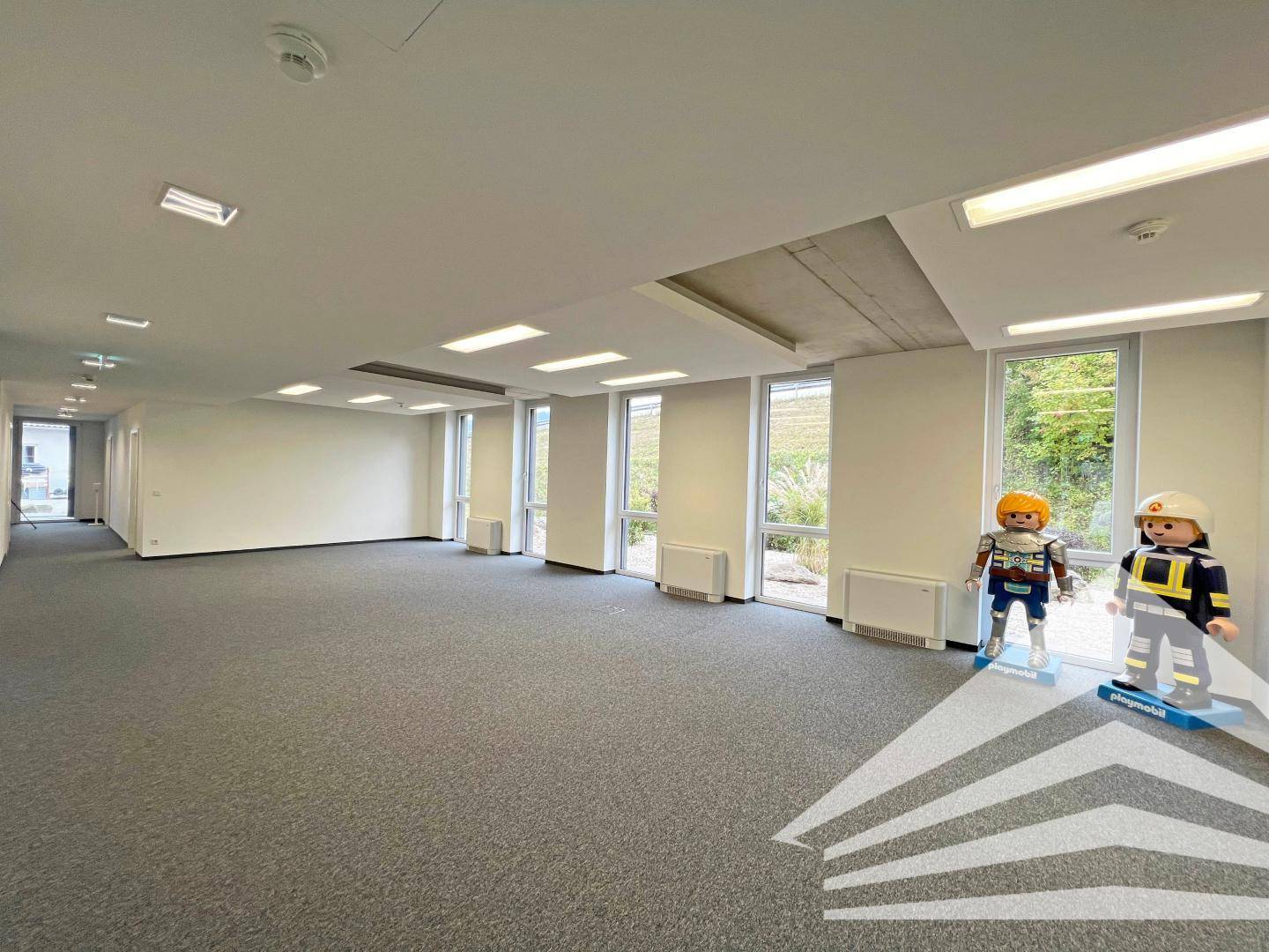 Großes, offenes Büro mit Teppichboden, vielen Fenstern und Blick auf die umliegende Landschaft, bereit zur individuellen Einrichtung.
