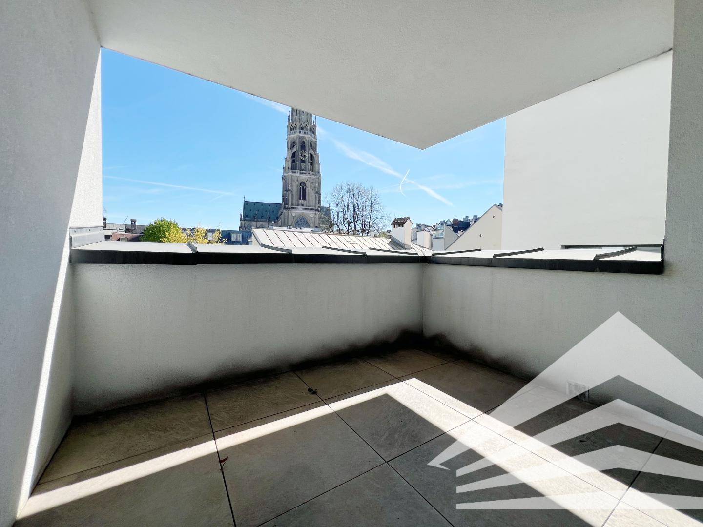 Geräumiger Balkon mit Fliesenboden und Blick auf eine historische Kirche unter blauem Himmel.