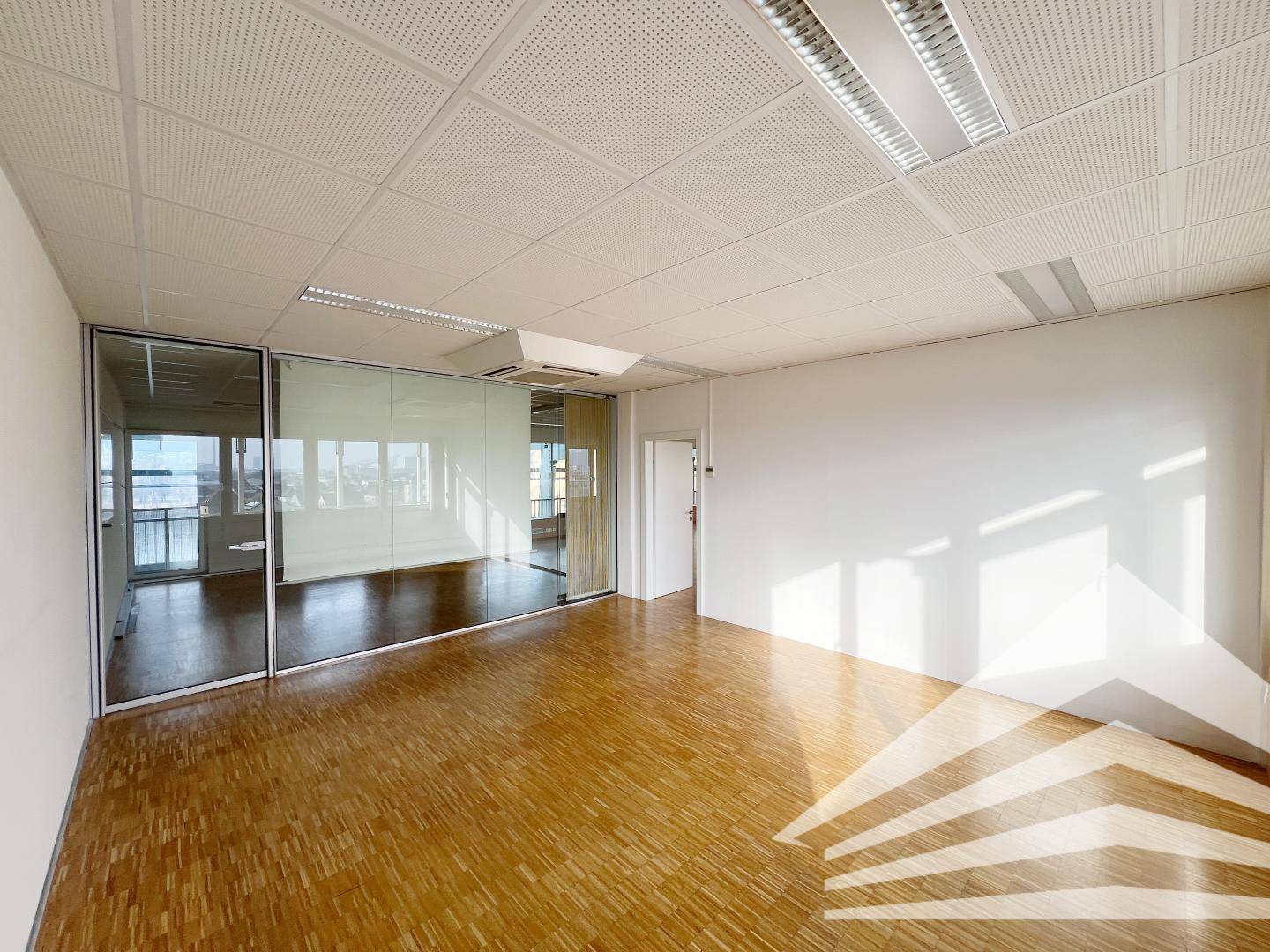 Moderner Büroraum mit Glaswänden, Parkettboden und viel Tageslicht, ideal für Besprechungen.