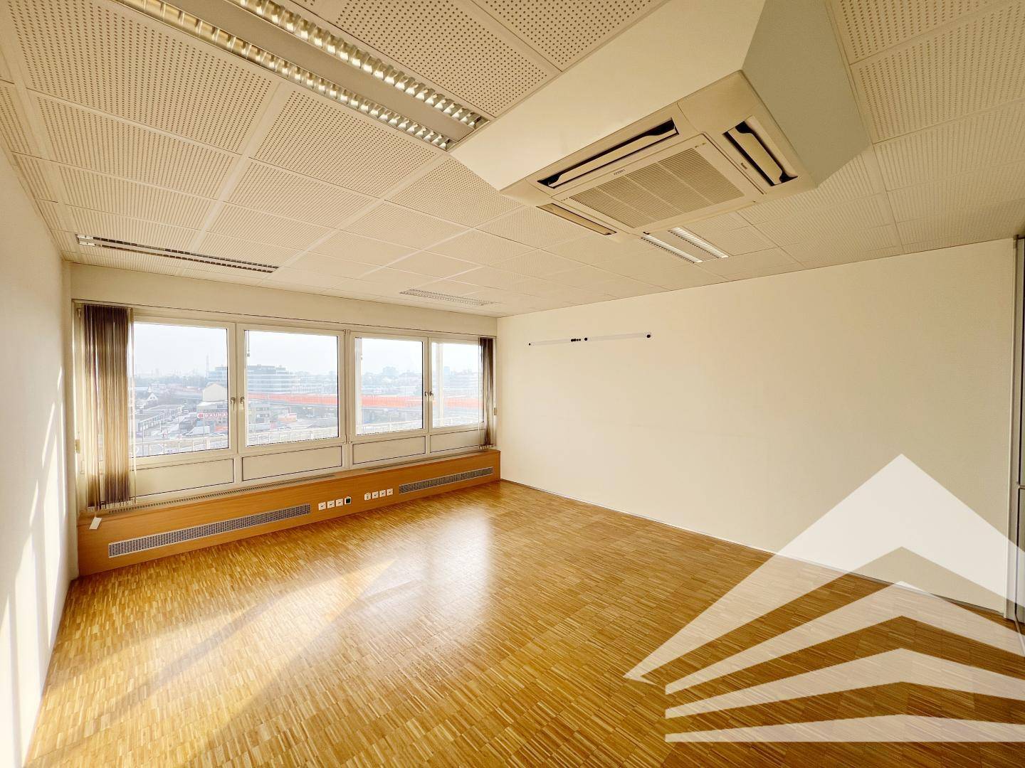 Bürofläche mit Parkettboden und breiter Fensterfront, die einen weiten Blick über die Stadt ermöglicht.