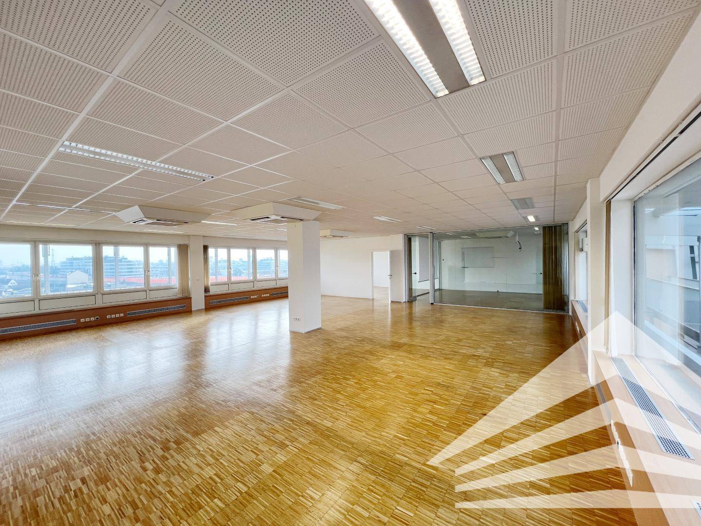 Weitläufiges Büro mit Holzparkett und einer Reihe von Fenstern, die einen Blick nach draußen bieten.