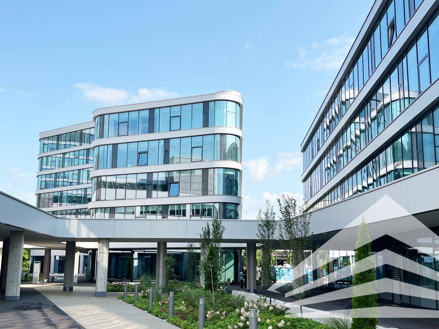 Mehrere moderne Bürogebäude mit geschwungenen Glasfassaden und einem überdachten Verbindungsgang.