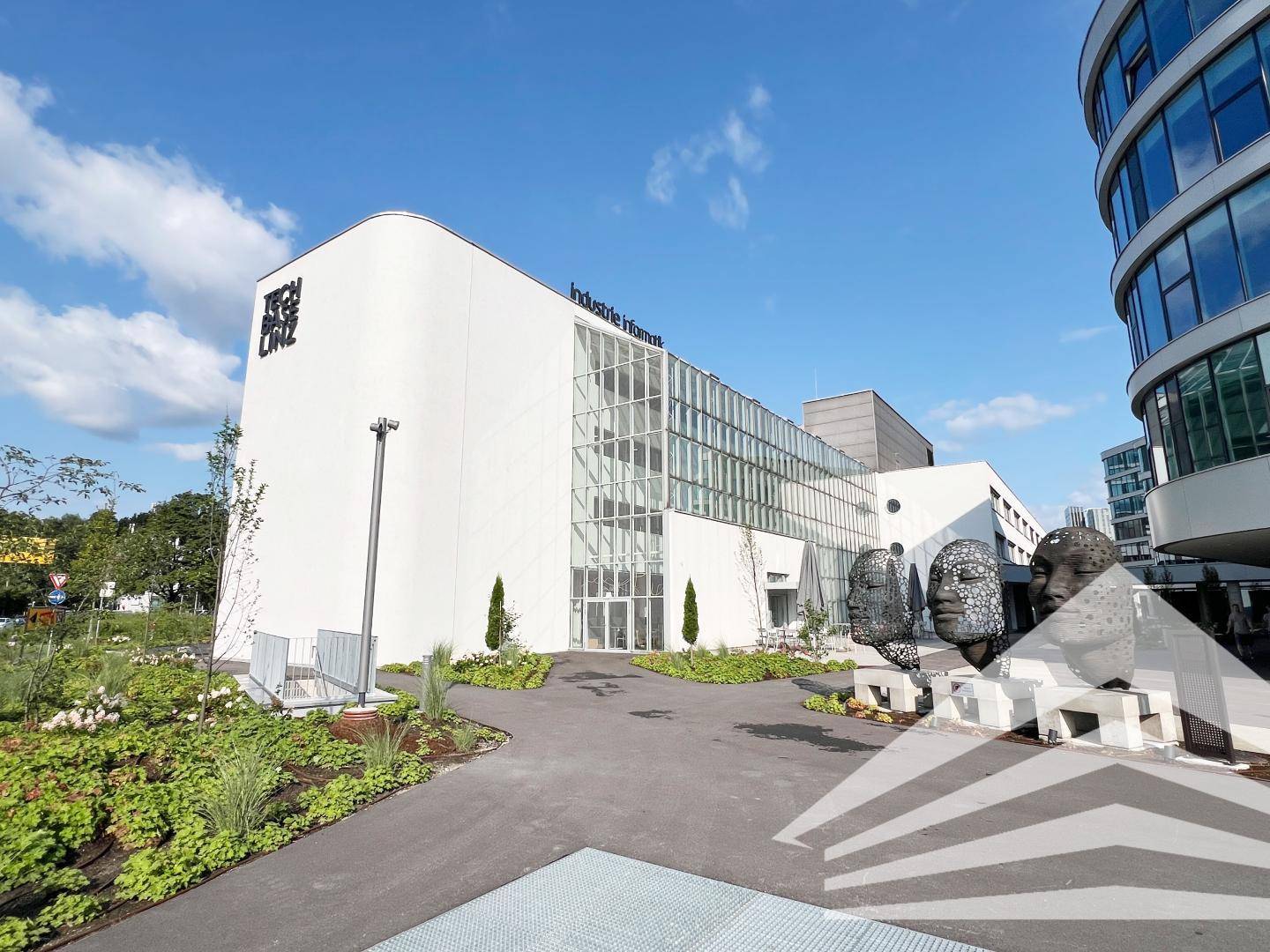 Zeitgenössisches Bürogebäude mit Glasfassade und Skulpturen im Eingangsbereich unter strahlendem Himmel.