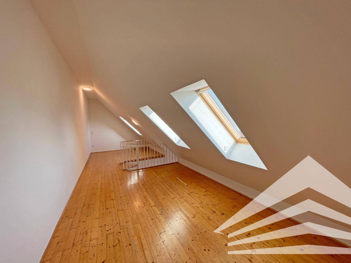 Langer Dachbodenraum mit Holzboden, mehreren Dachfenstern und schrägen Wänden.