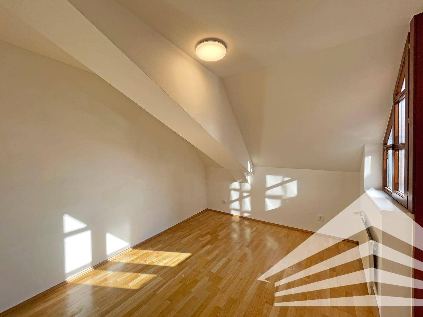 Gemütliches Zimmer im Dachgeschoss mit Holzboden, schrägen Wänden und viel Tageslicht.