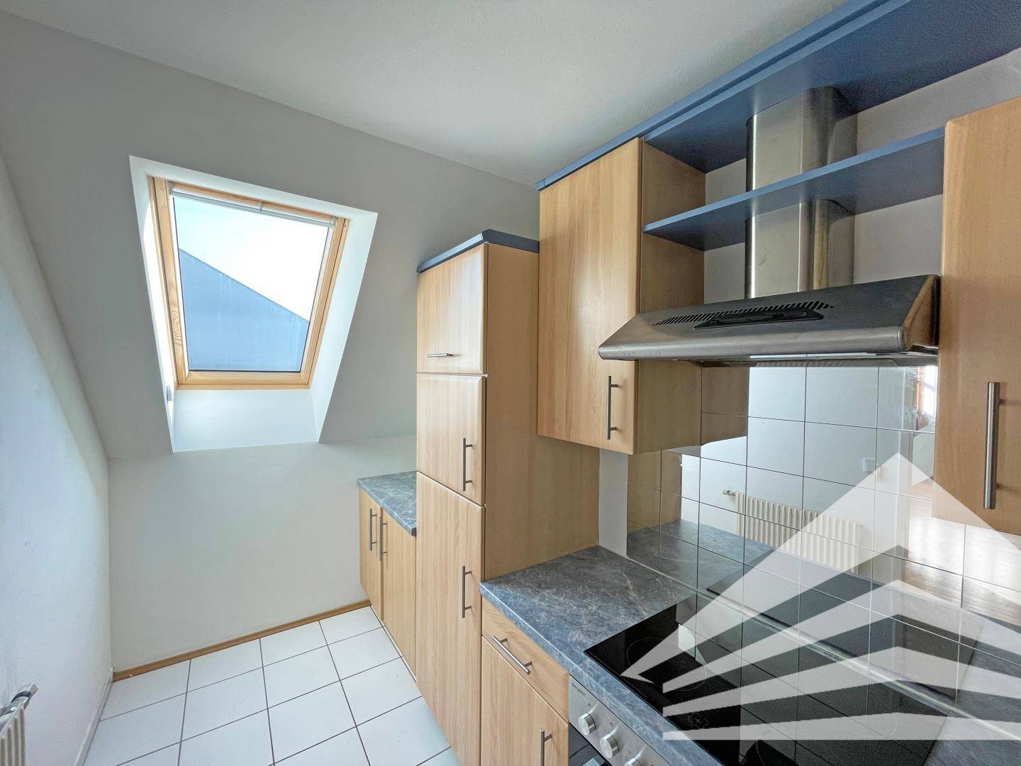 Helle Küche im Dachgeschoss mit Dachfenster, Holzschränken und Kochfeld.