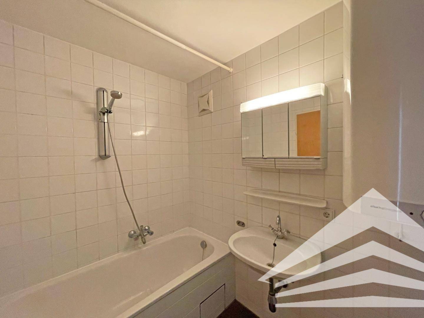 Gefliestes Badezimmer mit Badewanne, Dusche und Spiegelschrank in hellem Design.