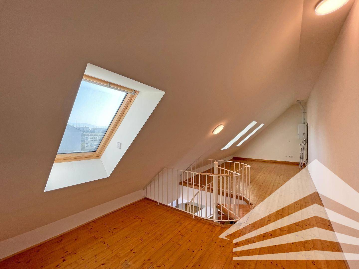 Geräumiger Dachbodenbereich mit Holzboden, Wendeltreppe und großem Dachfenster.
