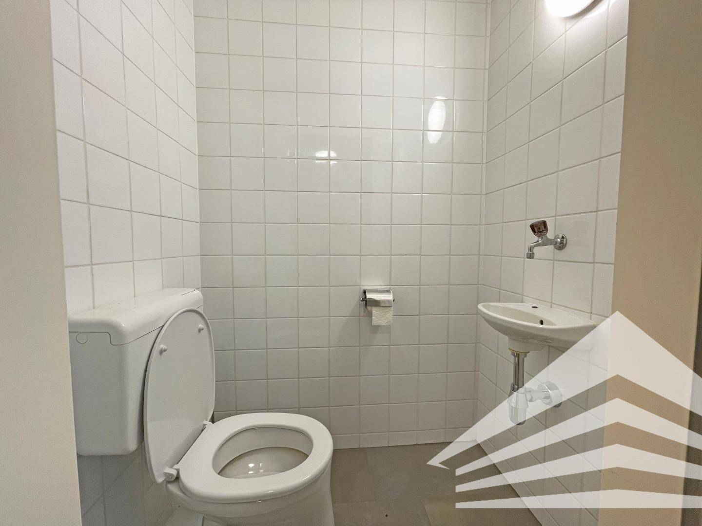 Separates WC mit weißer Toilette, Waschbecken und hellen Wandfliesen.