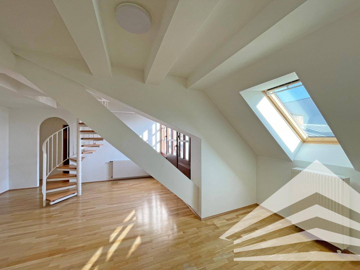 Heller Dachbodenraum mit Holzparkett, schrägen Wänden und einer Wendeltreppe.