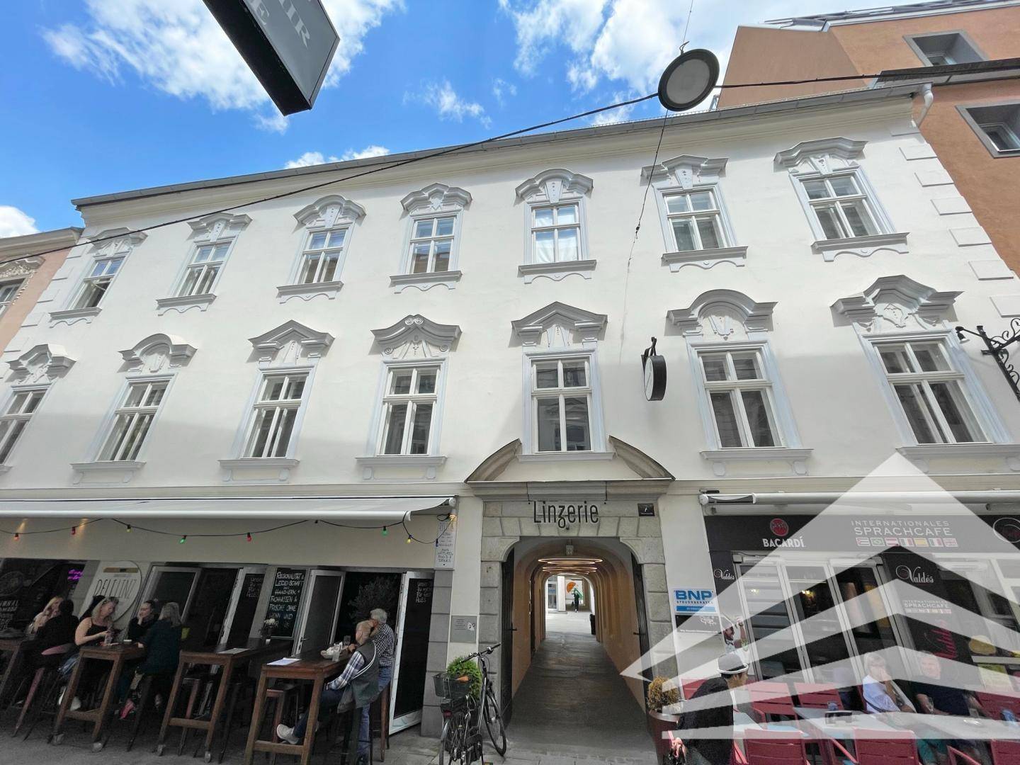 Historische Fassade eines Gebäudes mit Geschäften im Erdgeschoss und dekorativen Fenstern.