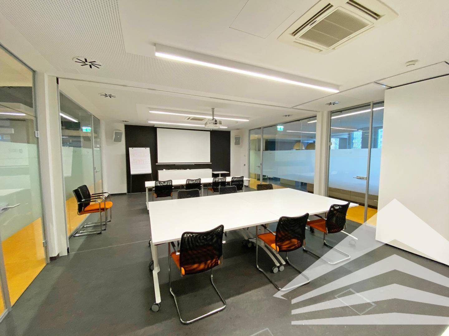 Großer Konferenzraum mit Beamer, Leinwand und flexiblen Tischen für Präsentationen und Workshops.