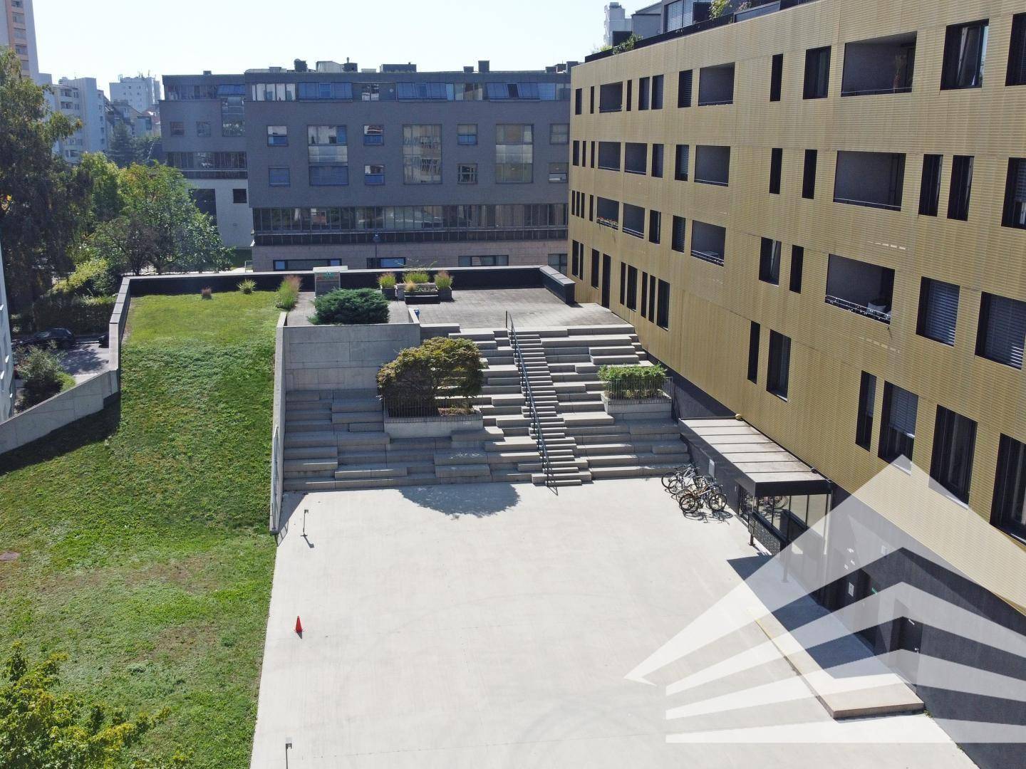 Weitläufiger Innenhof mit Treppenstufen, Grünflächen und Fahrradabstellplätzen zwischen Gebäuden.