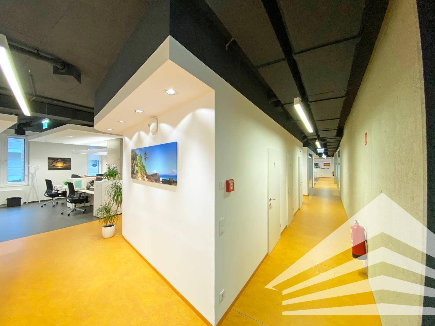 Langer Bürogang mit gelbem Boden, weißen Wänden und Blick in offene Büroräume mit moderner Einrichtung.
