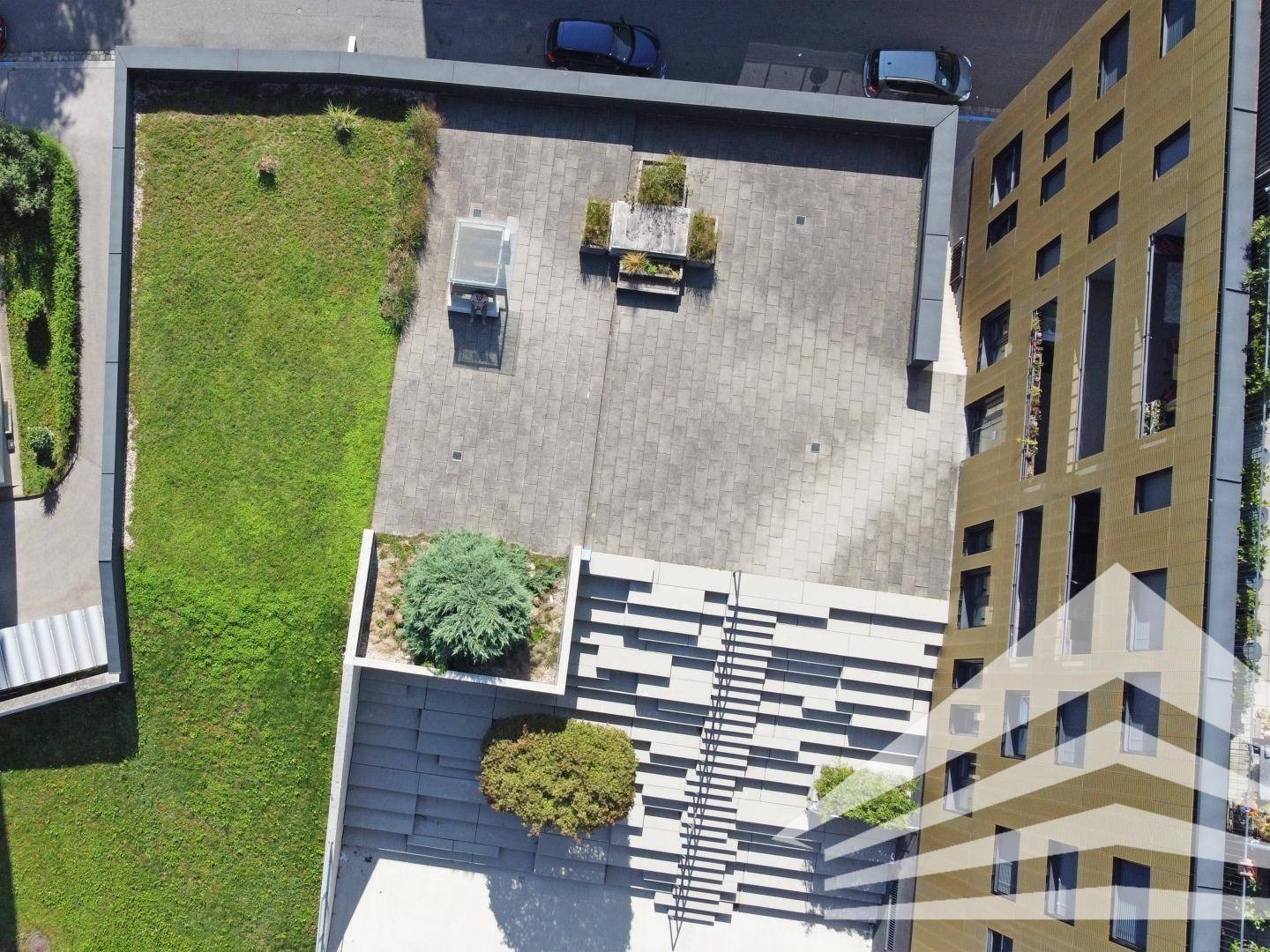 Dachterrasse mit Sitzgelegenheiten, Grünflächen und modernen Landschaftselementen von oben betrachtet.