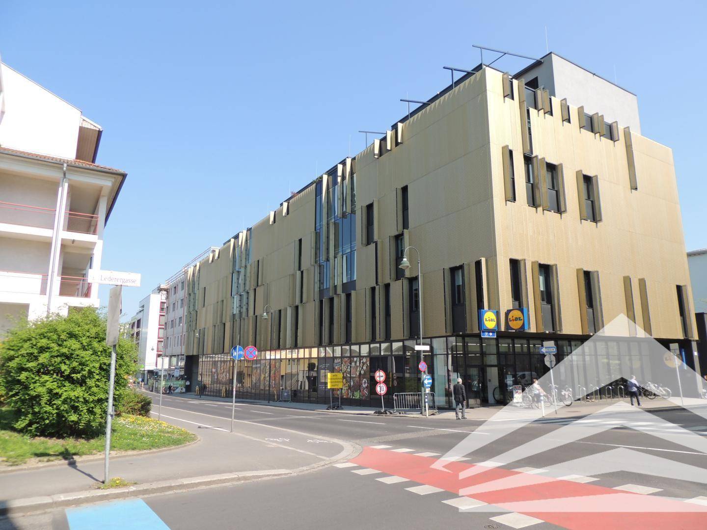Straßenansicht des modernen Gebäudes mit goldener Fassade, großen Fenstern und Einzelhandelsgeschäften im Erdgeschoss.