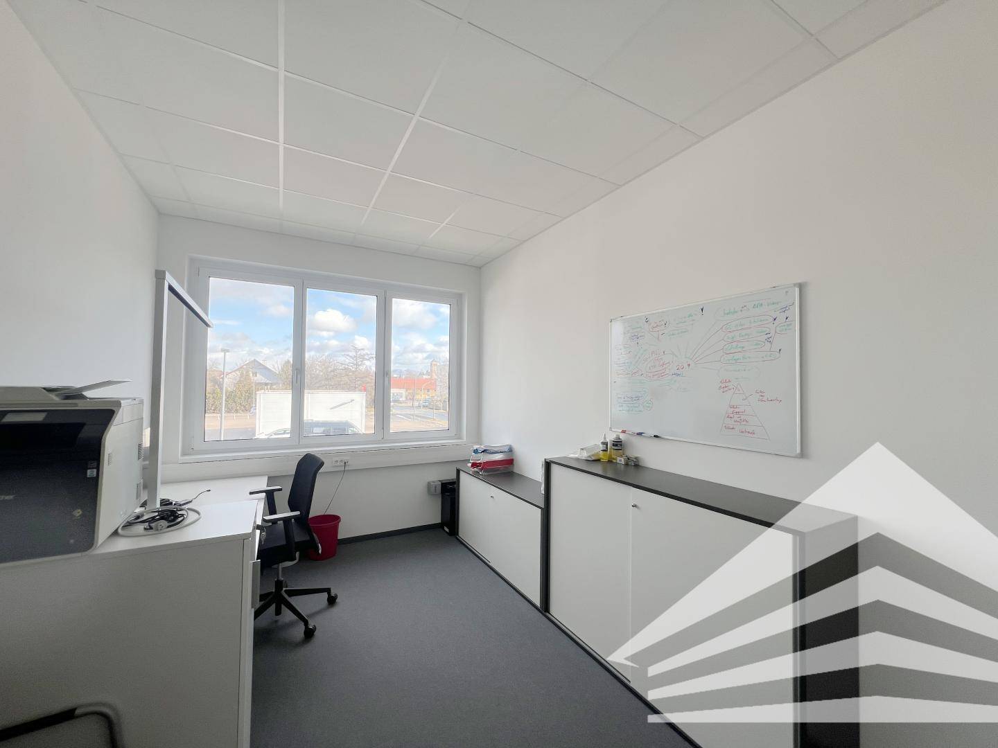 Helles Einzelbüro mit großem Fenster, Schreibtisch und Whiteboard an der Wand.