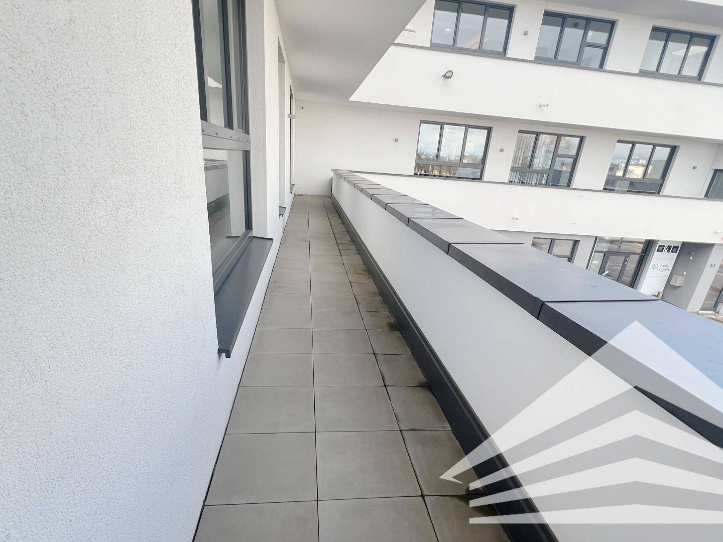 Langer Balkon mit Fliesenboden und Blick auf das moderne Bürogebäude.
