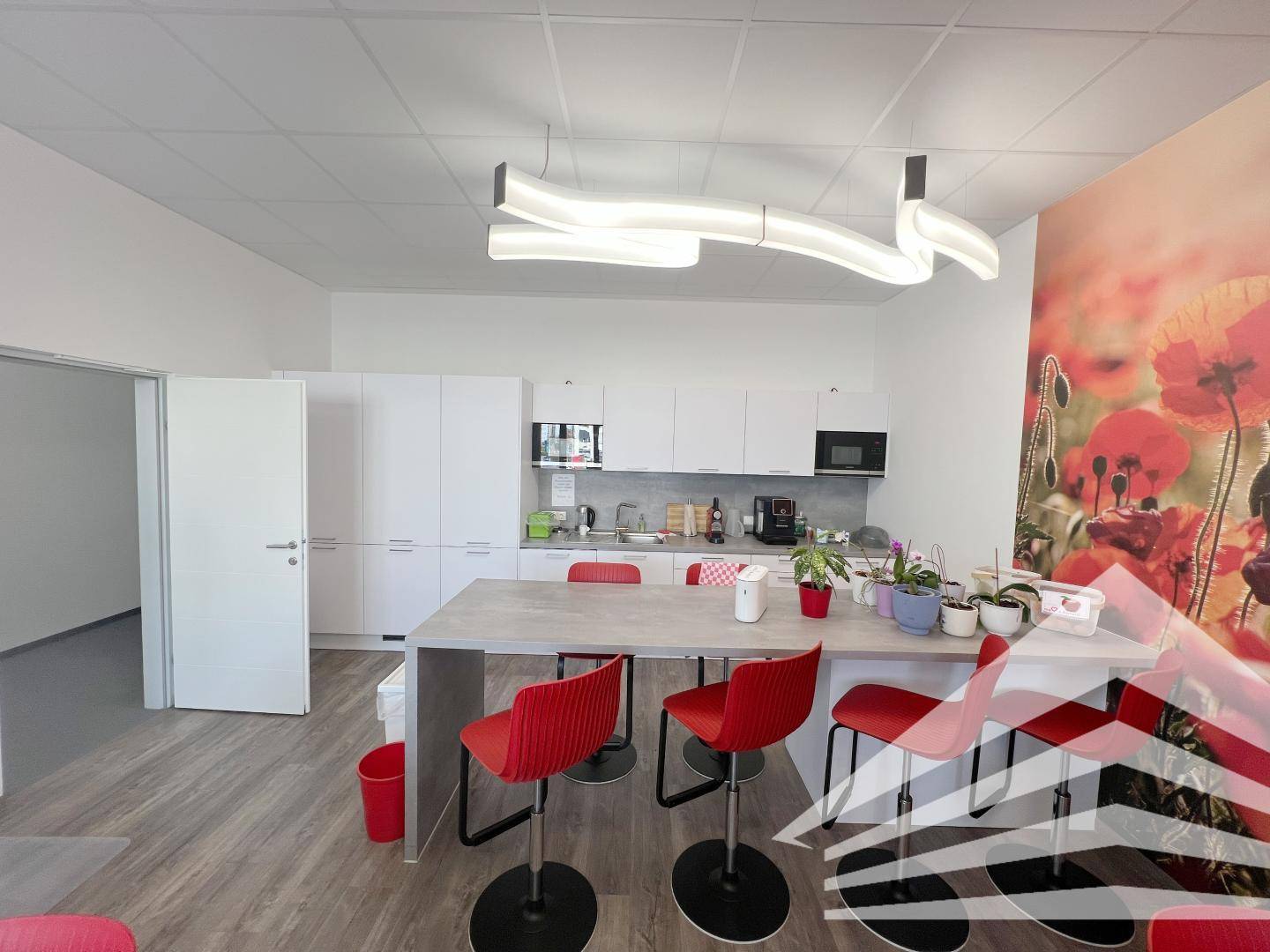Helle Büroküche mit weißen Schränken, einer roten Akzentwand und modernen Barhockern.