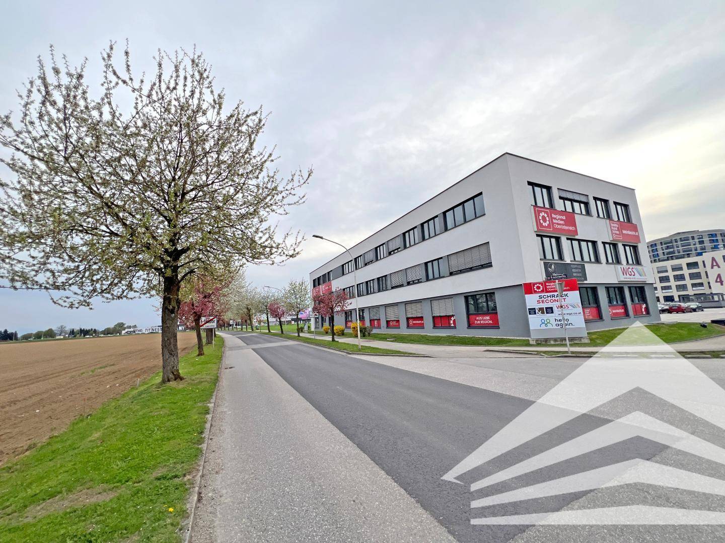 Modernes Bürogebäude an einer Straße, umgeben von Bäumen und Feldern.