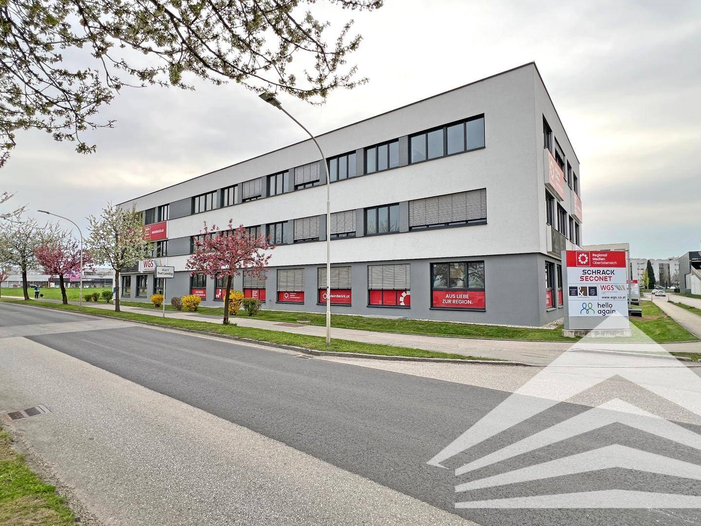 Modernes Bürogebäude an einer Straße mit großen Fenstern und Werbeschildern.