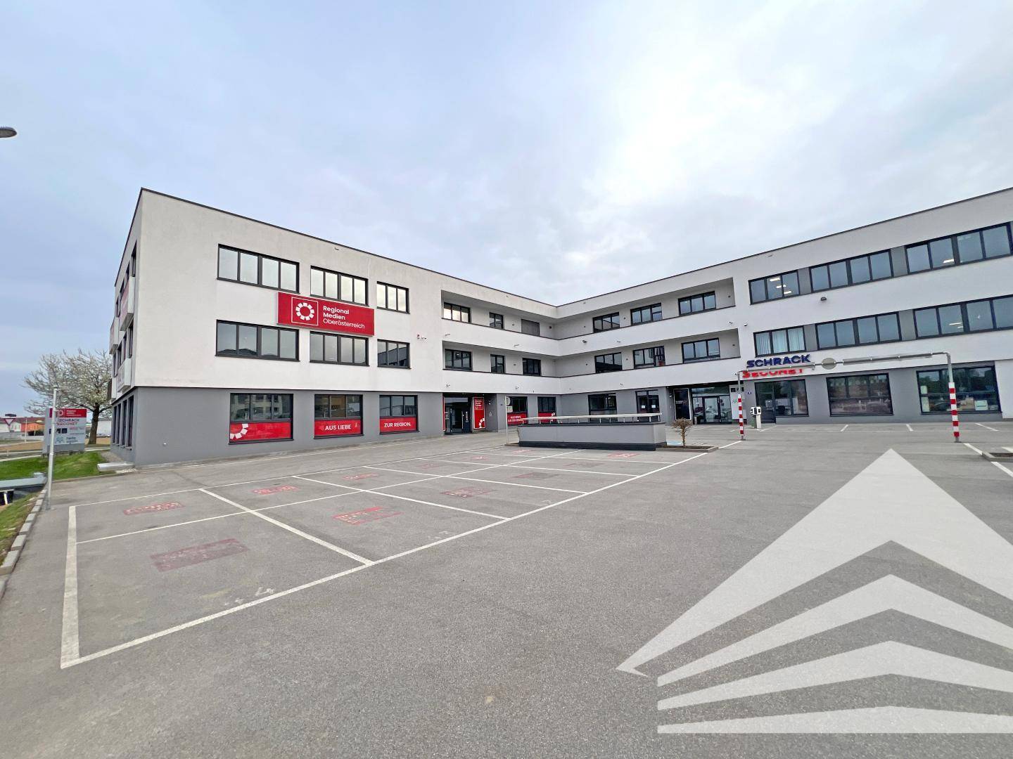 Modernes Bürogebäude mit großem Parkplatz und umliegenden Geschäftsflächen.