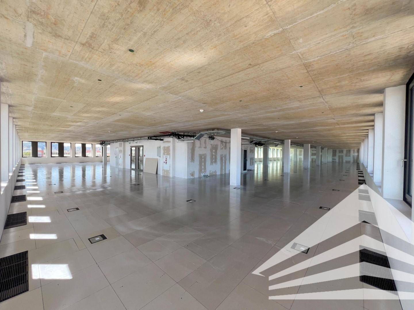 Weitläufiger, offener Bürobereich mit Sichtbetondecke, Fliesenboden und großen Fenstern, bereit für den Ausbau.