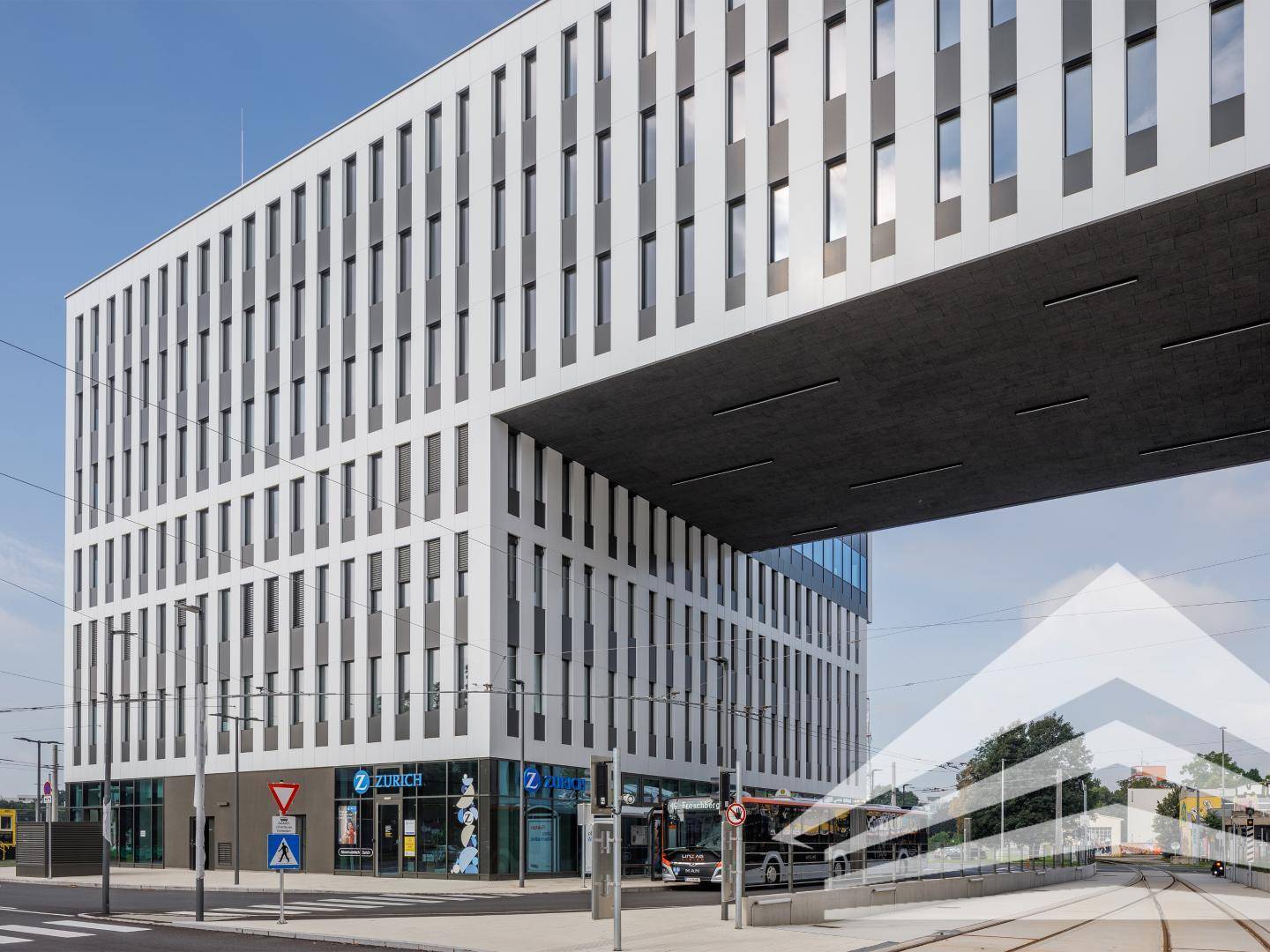 Modernes Bürogebäude mit weißer Fassade und dunklen Akzenten an einer belebten Straße mit öffentlichen Verkehrsmitteln.