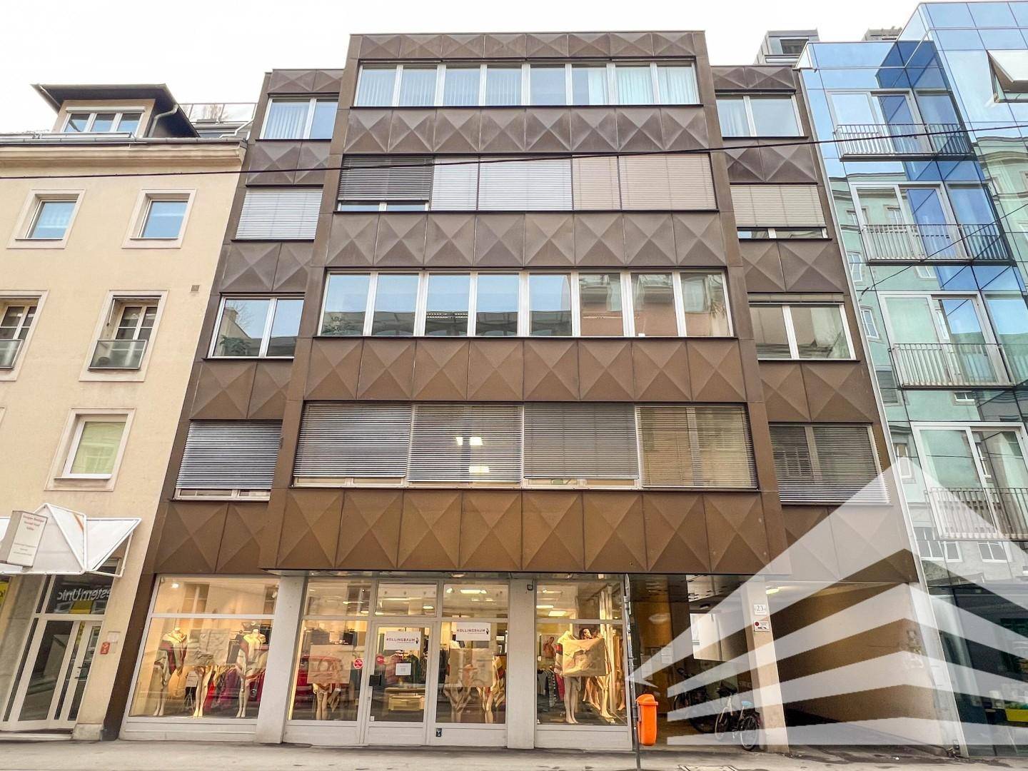 Modernes Geschäftsgebäude mit markanter brauner Fassade, großen Fenstern und Ladenflächen im Erdgeschoss.