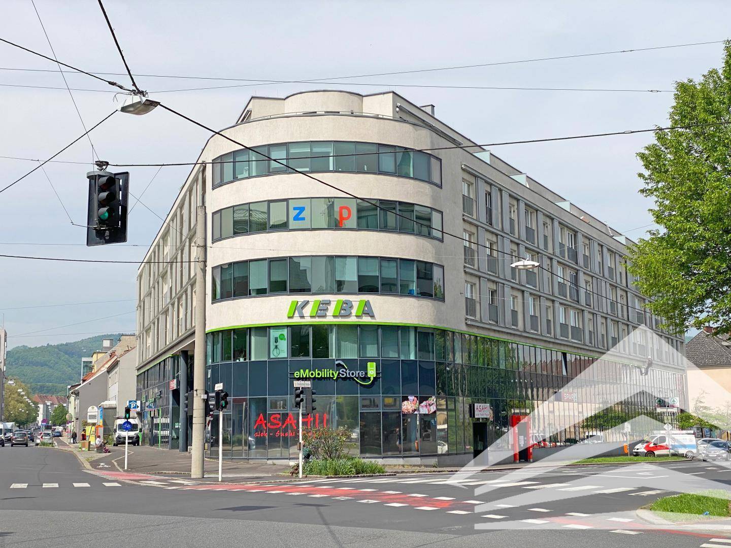 Modernes Geschäftsgebäude an einer Straßenecke mit geschwungener Fassade, großen Glasflächen und urbaner Umgebung.