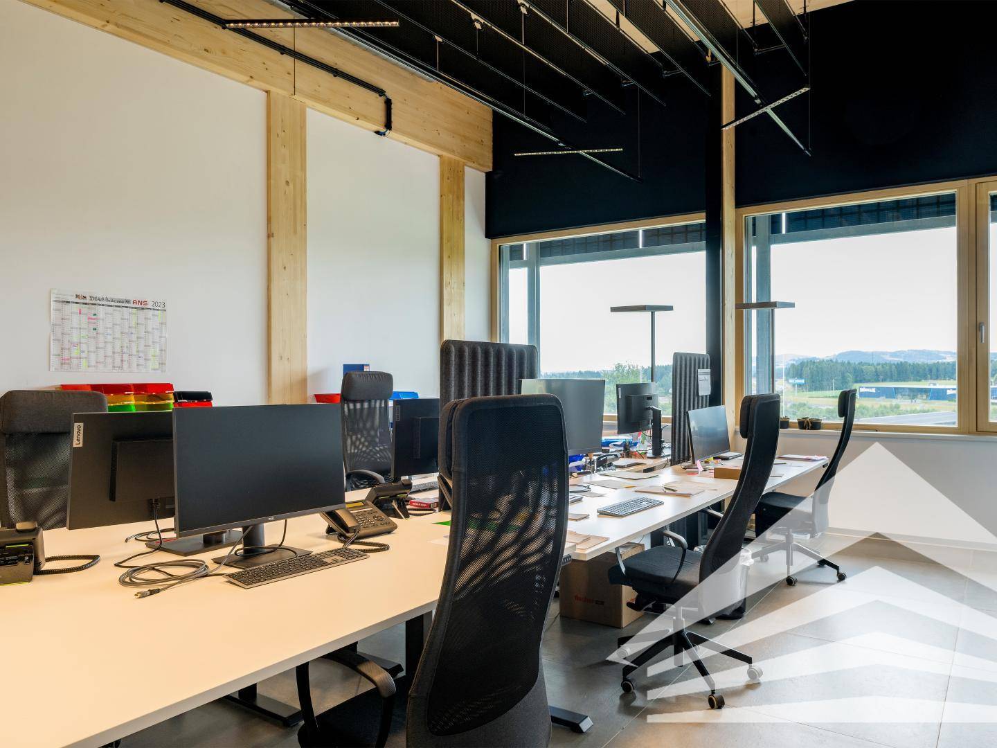 Offener Bürobereich mit mehreren Arbeitsplätzen, großen Fenstern und Blick auf die Landschaft.