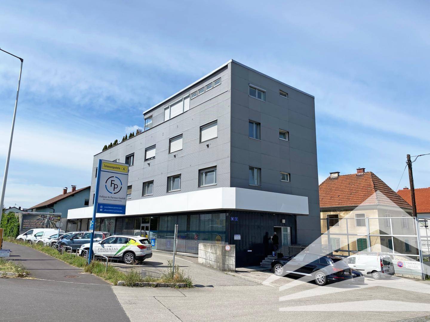 Modernes Geschäftsgebäude mit grauer Fassade, großen Fenstern und Parkplätzen davor.