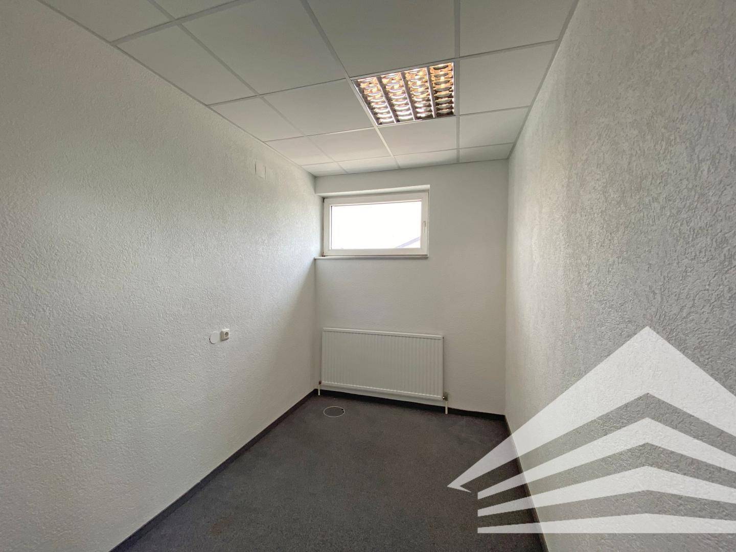 Kleineres, leeres Büro mit Teppichboden, strukturierten Wänden und einem Fenster.