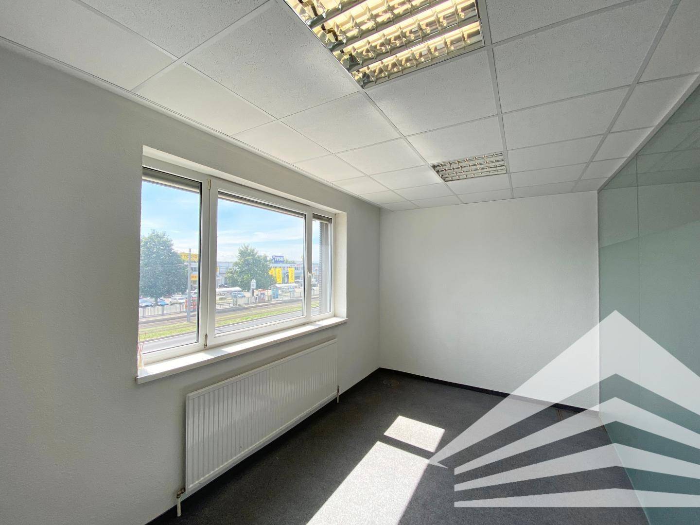 Helles, leeres Büro mit Teppichboden, großem Fenster und Blick auf die Stadt.