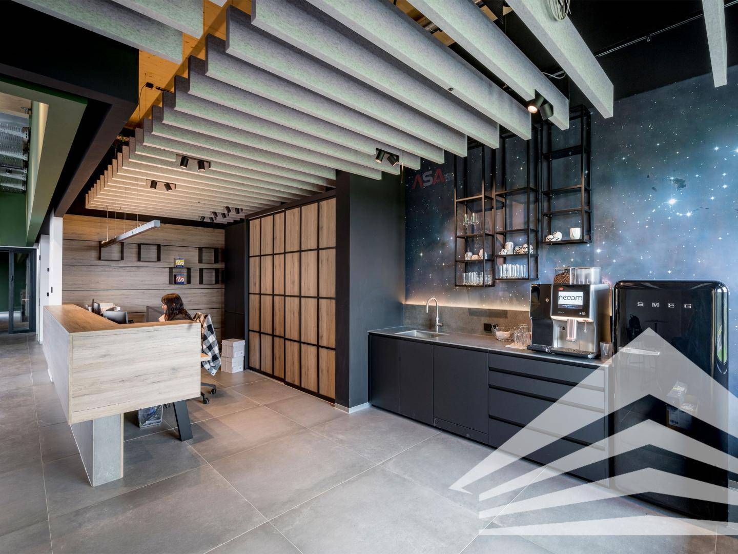 Moderne Büroküche mit dunkler Arbeitsplatte, Spüle, Kaffeemaschine und einem Retro-Kühlschrank vor einer Sternenwand.