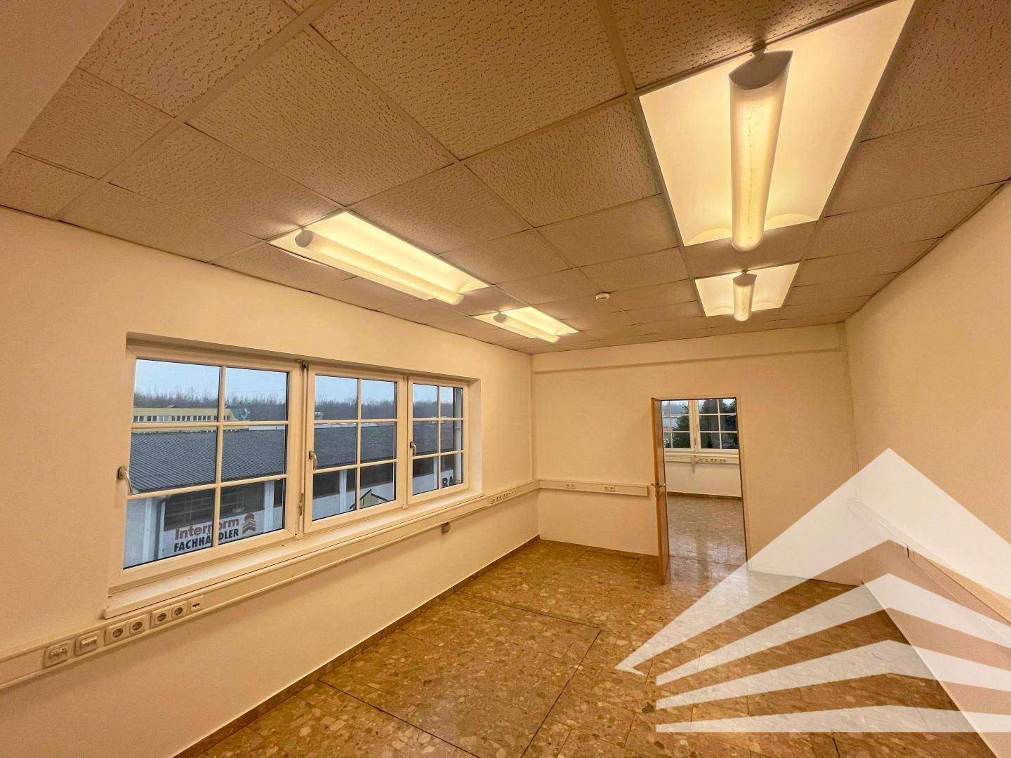 Geräumiges Büro mit Fliesenboden und Blick durch eine Tür in einen angrenzenden Raum.