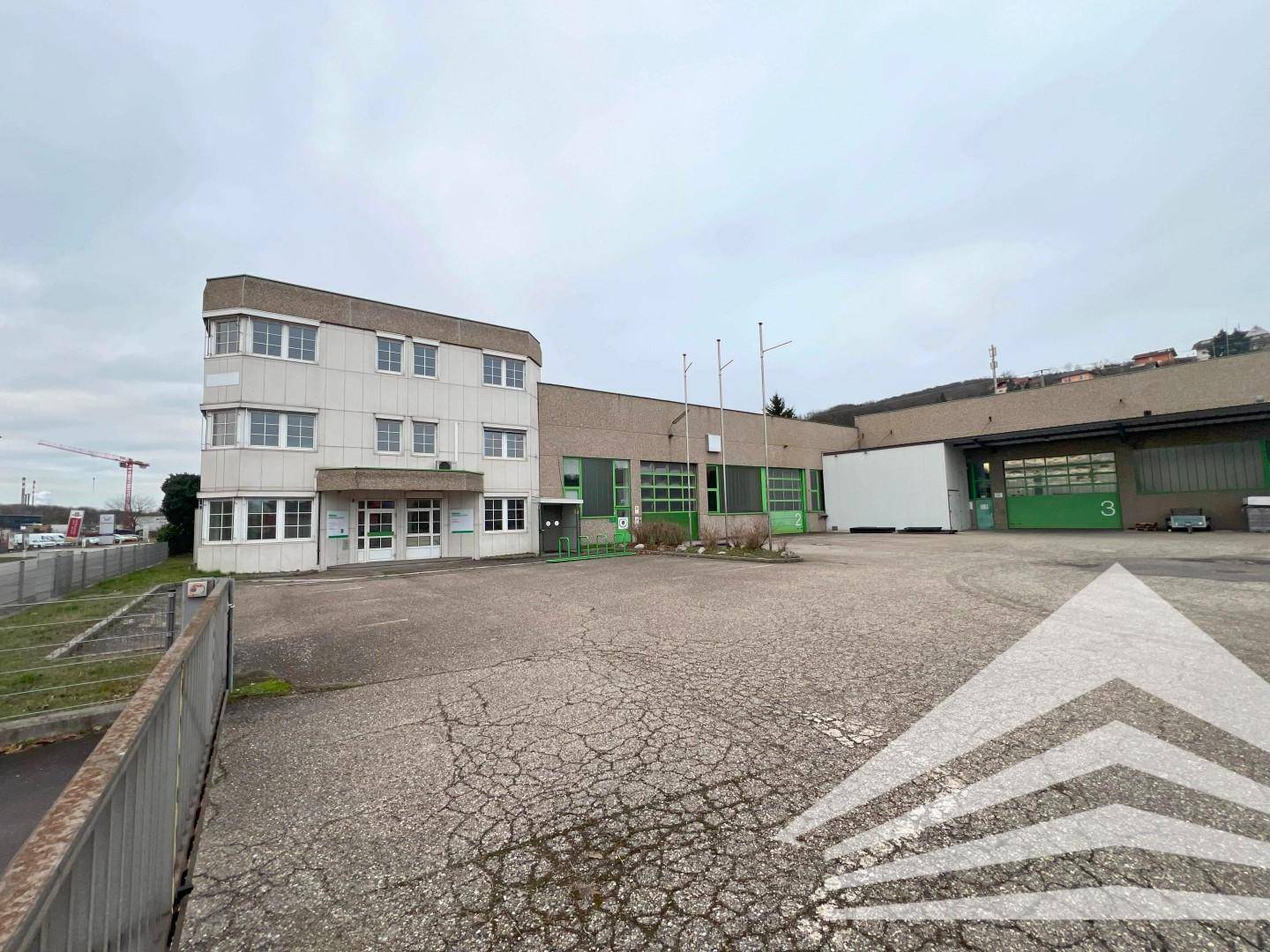 Weitläufige Außenansicht eines Gewerbekomplexes mit Bürogebäude und angrenzenden Hallenbereichen.