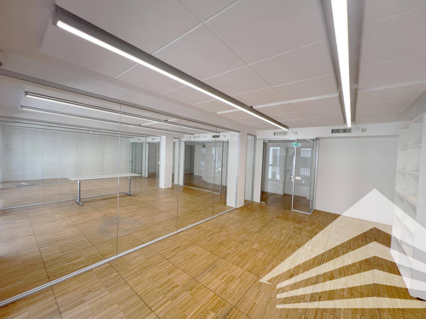 Flexibles Bürokonzept mit Glaswänden, Holzparkett und moderner Beleuchtung, ideal für verschiedene Arbeitsbereiche.