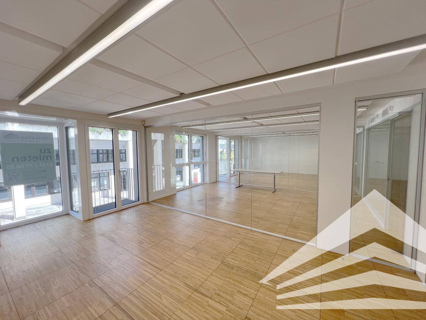 Modernes Büro mit großen Fensterfronten, Holzfußboden und integrierten Glaswänden für flexible Raumgestaltung.