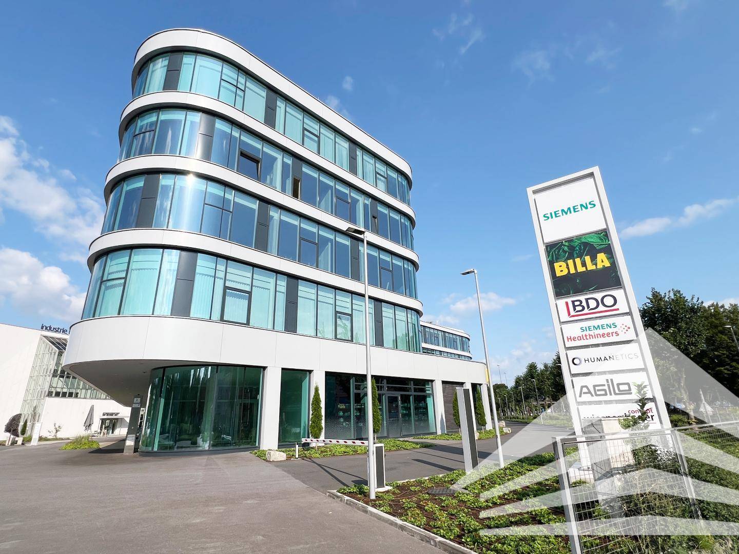 Modernes Bürogebäude mit geschwungener Glasfassade und einem großen Firmenschild im Außenbereich.