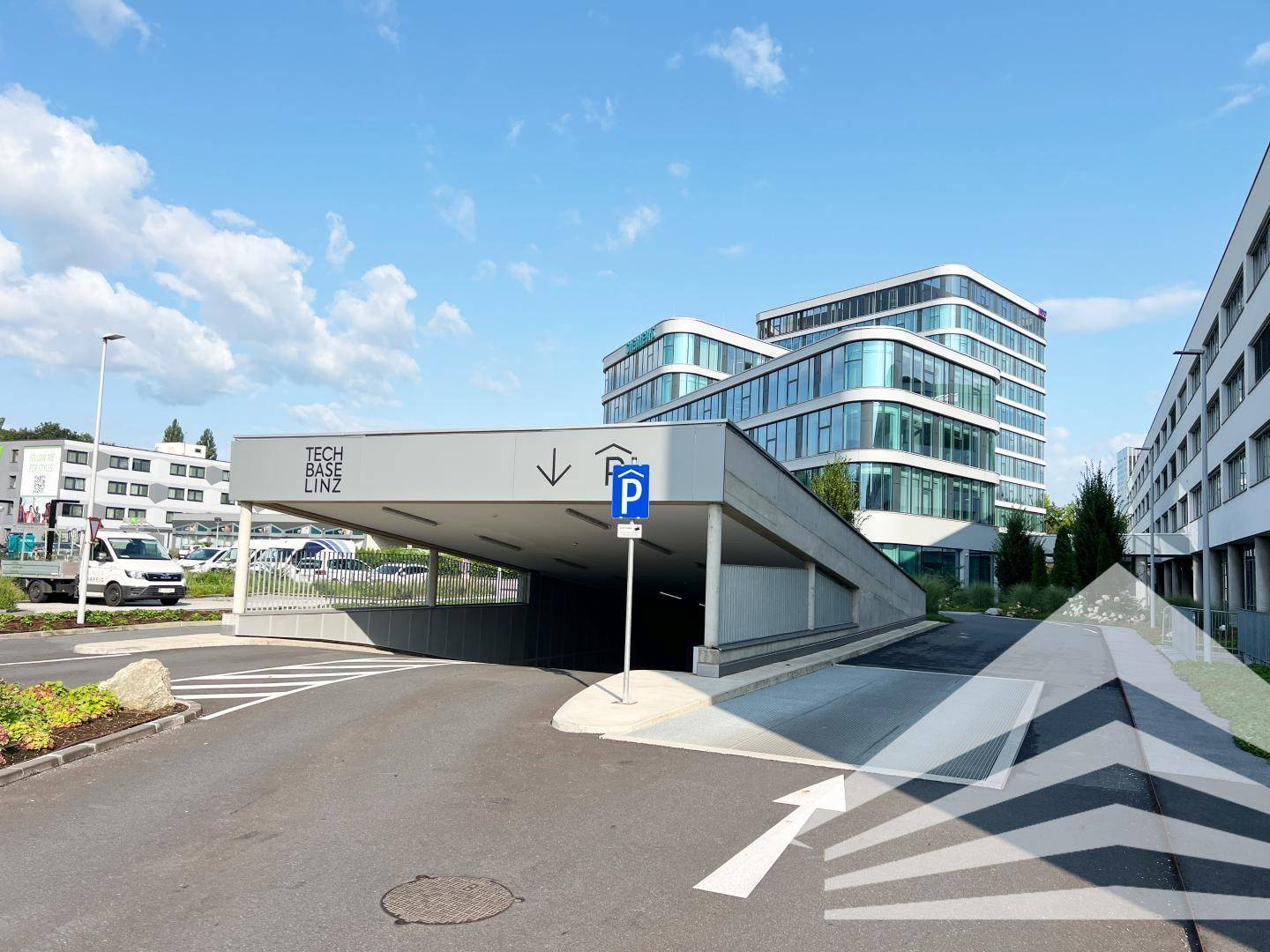Zufahrt zu einer Tiefgarage mit dem modernen Bürogebäude im Hintergrund unter blauem Himmel.