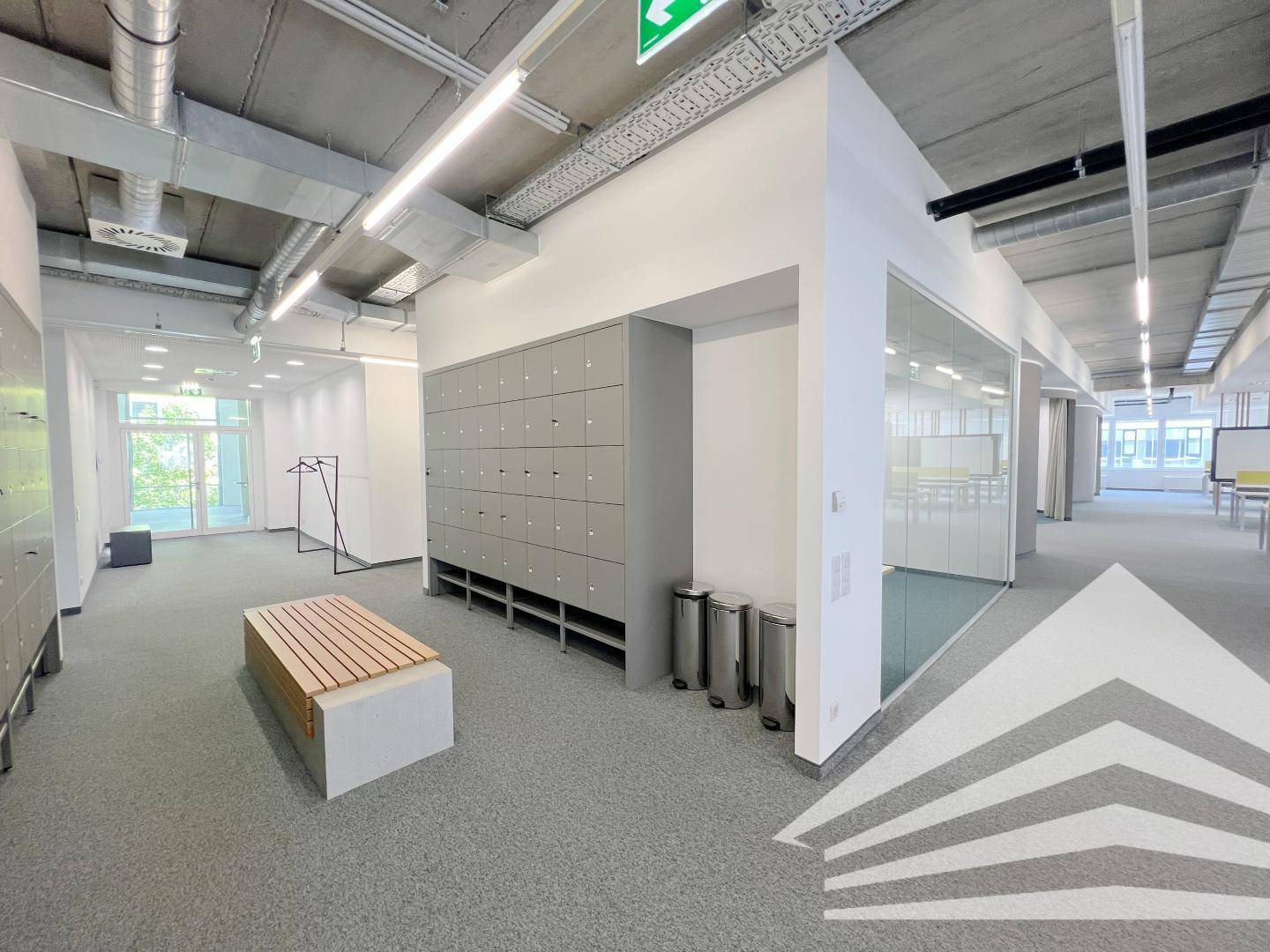 Bürobereich mit Schließfächern, einer Holzbank und Glaswänden zu weiteren Büroräumen.