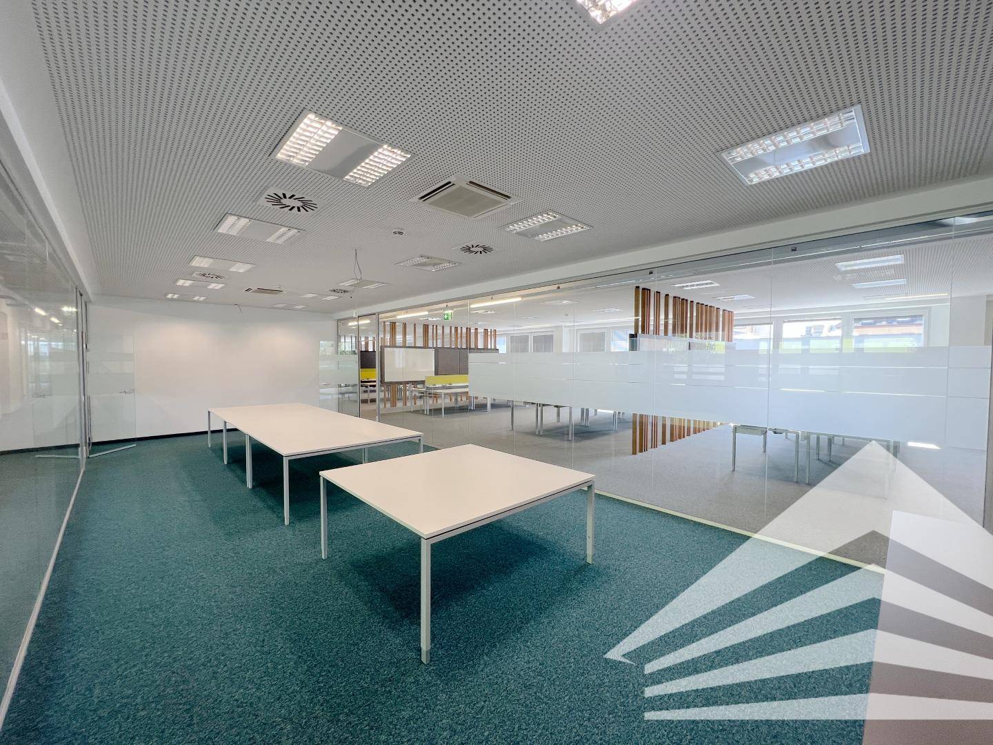 Besprechungsraum oder offener Bürobereich mit Tischen, Glaswänden und einer perforierten Decke.