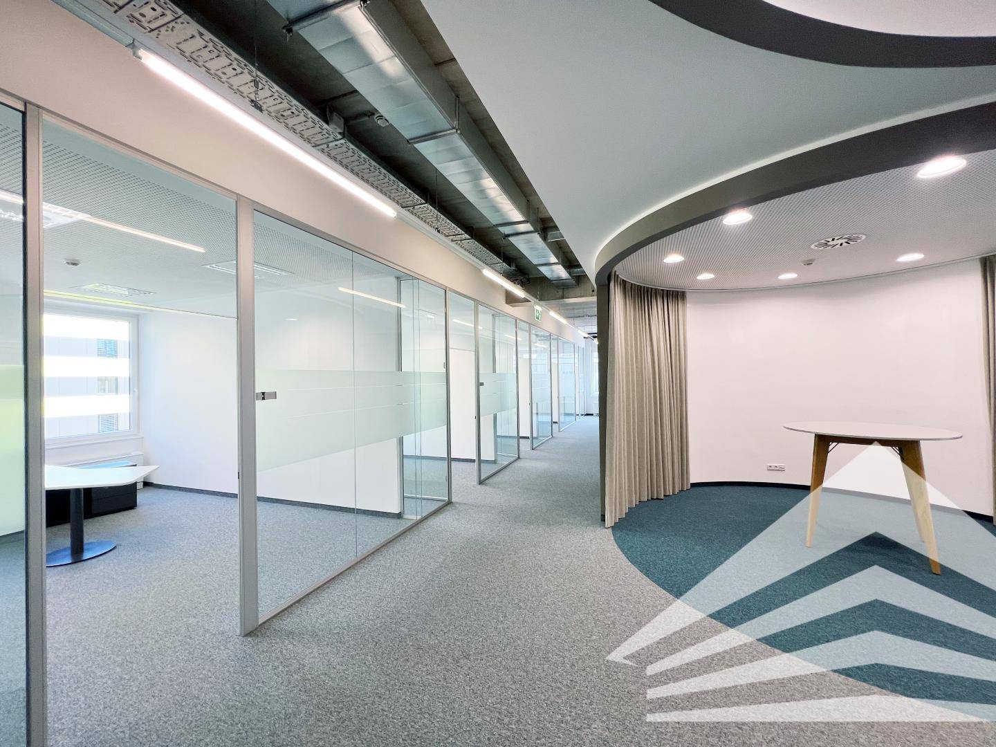 Moderner Büroflur mit Glasbüros und einer geschwungenen Wand, beleuchtet durch Deckenleuchten.