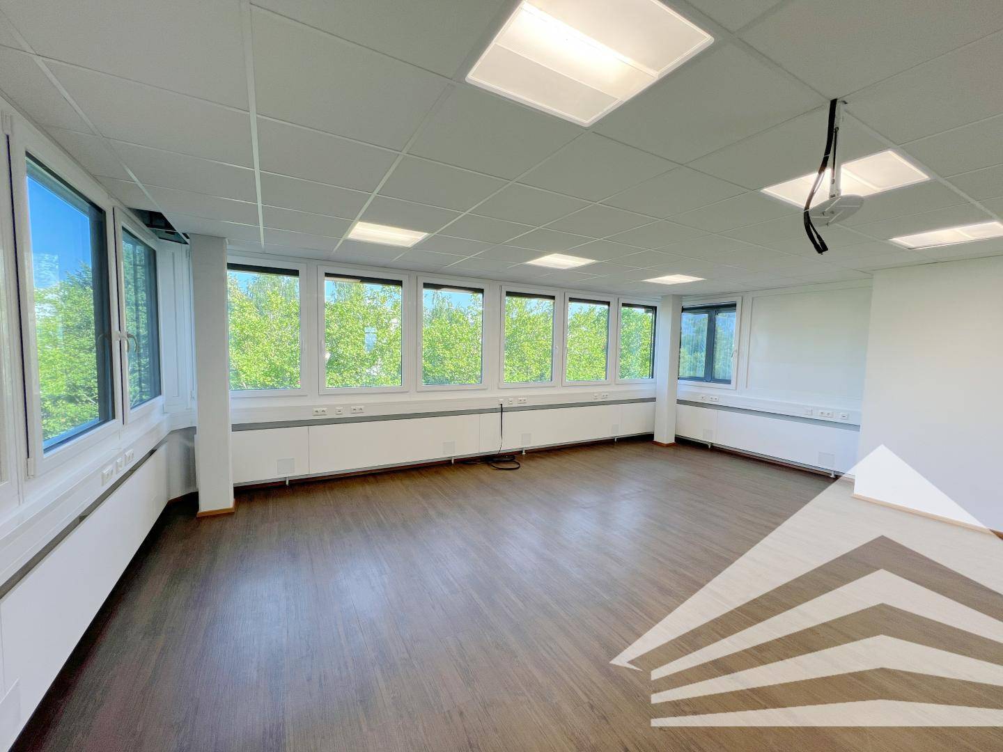 Helles Büro mit durchgehender Fensterfront und Blick auf Bäume, ausgestattet mit praktischem Laminatboden.