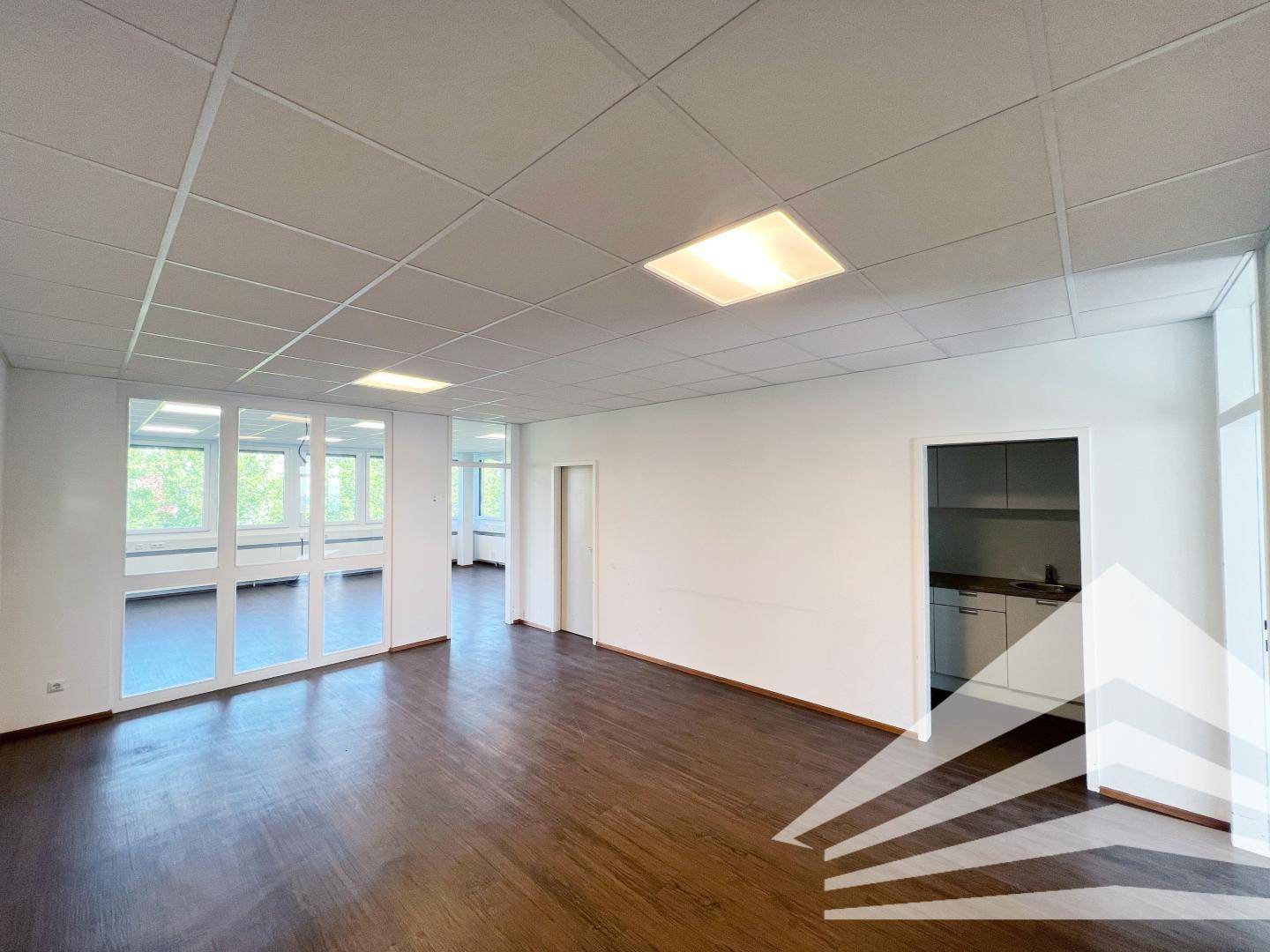 Großes Büro mit Glasabtrennung zu einem Nebenraum und Zugang zu einer kleinen Teeküche.