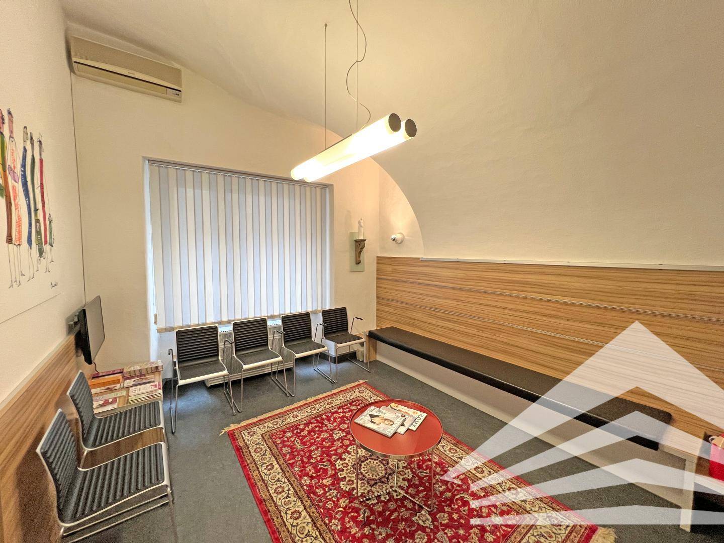 Wartezimmer mit bequemen Stühlen, einem roten Teppich und einer langen Sitzbank.