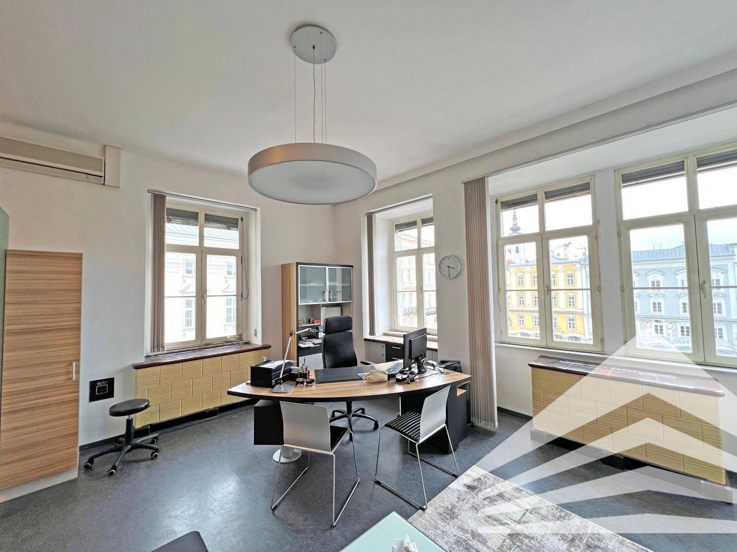 Geräumiges Büro mit großem Schreibtisch, Bürostuhl und mehreren Fenstern mit Stadtblick.